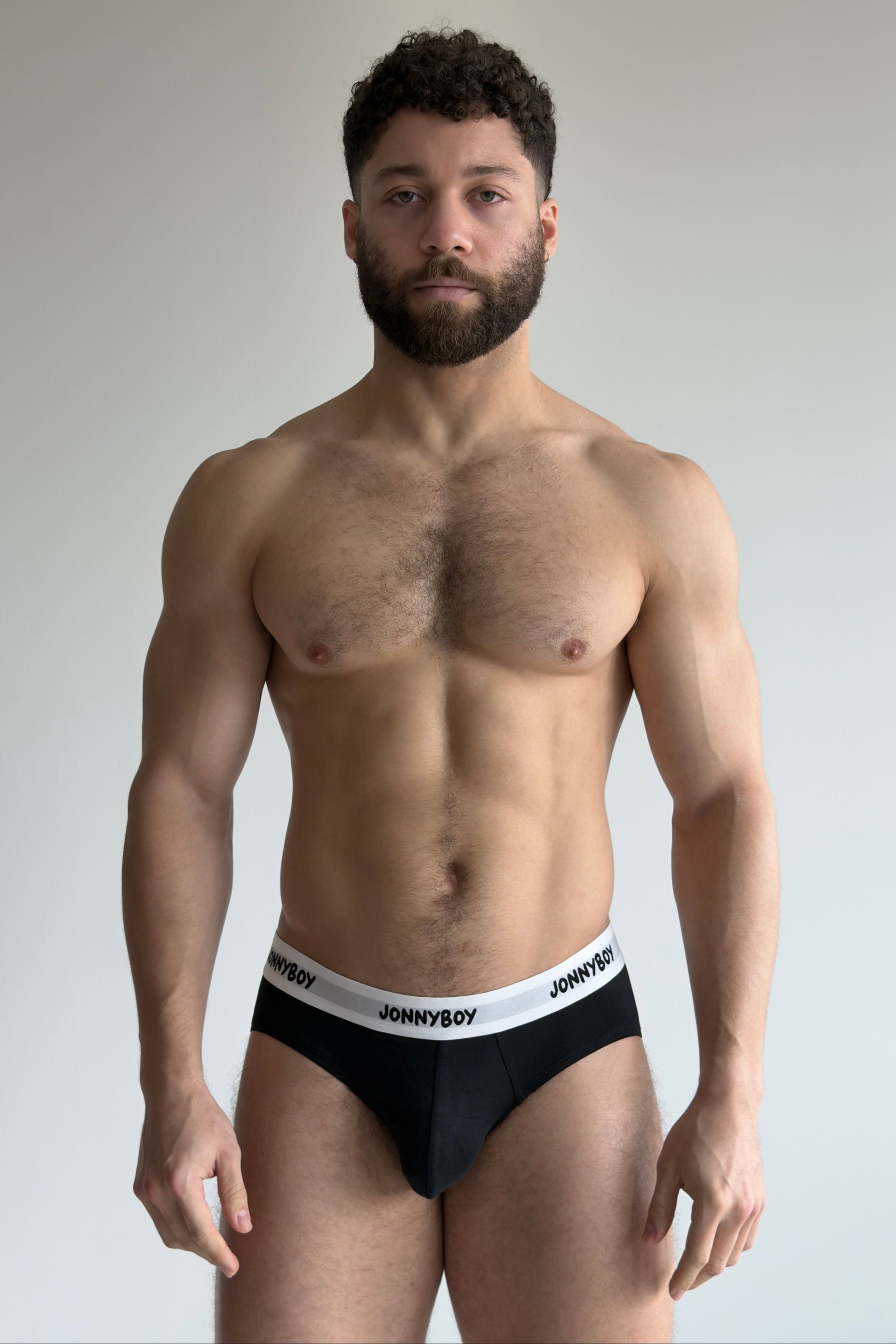Man wearing black underwear with 'JOHNNYBOY' waistband against a plain background