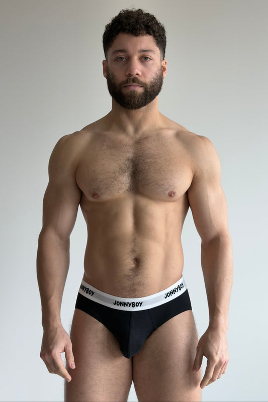 Man wearing black underwear with 'JOHNNYBOY' waistband against a plain background
