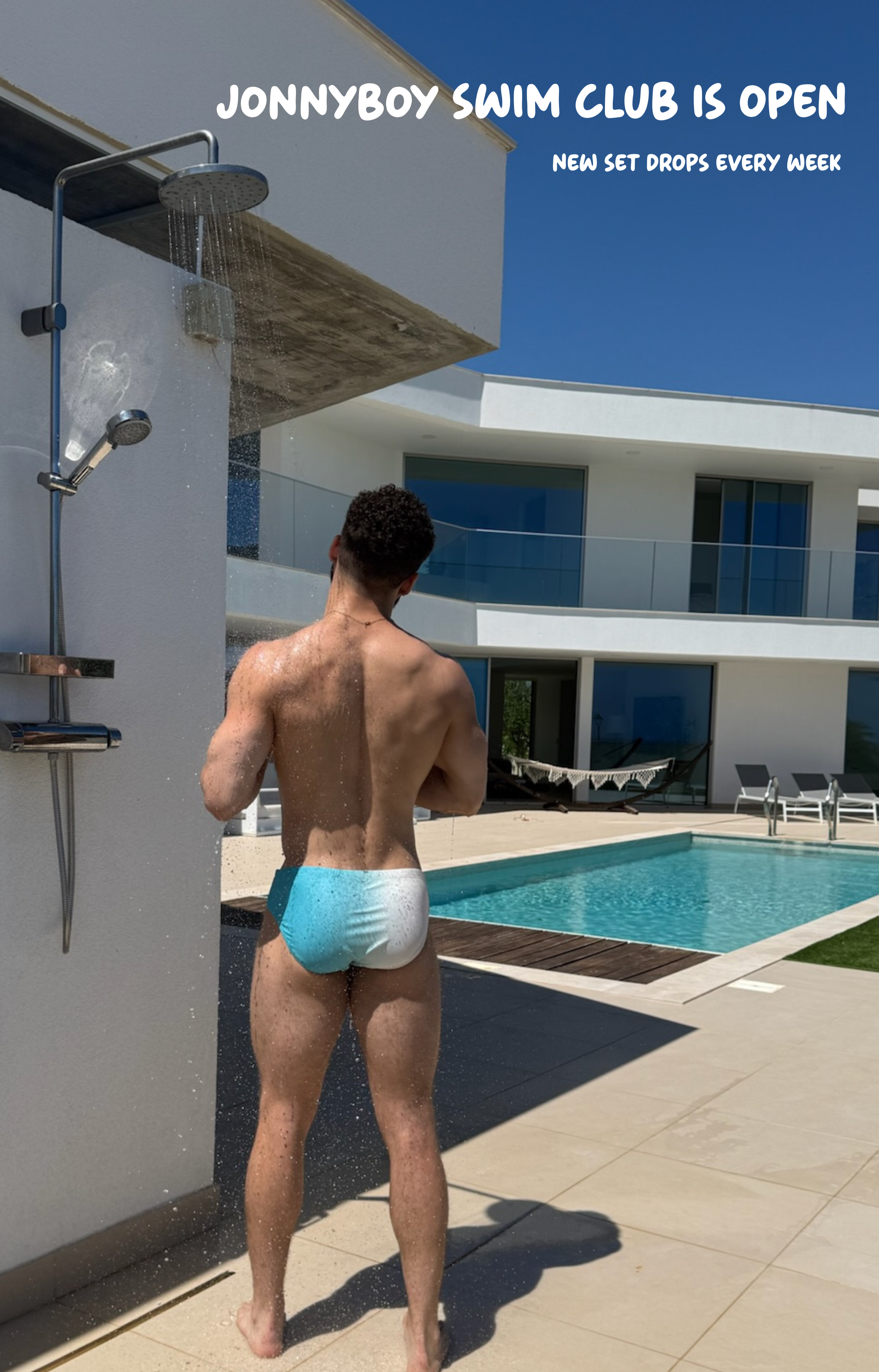 Man in blue swim trunks standing by a pool with modern building in the background